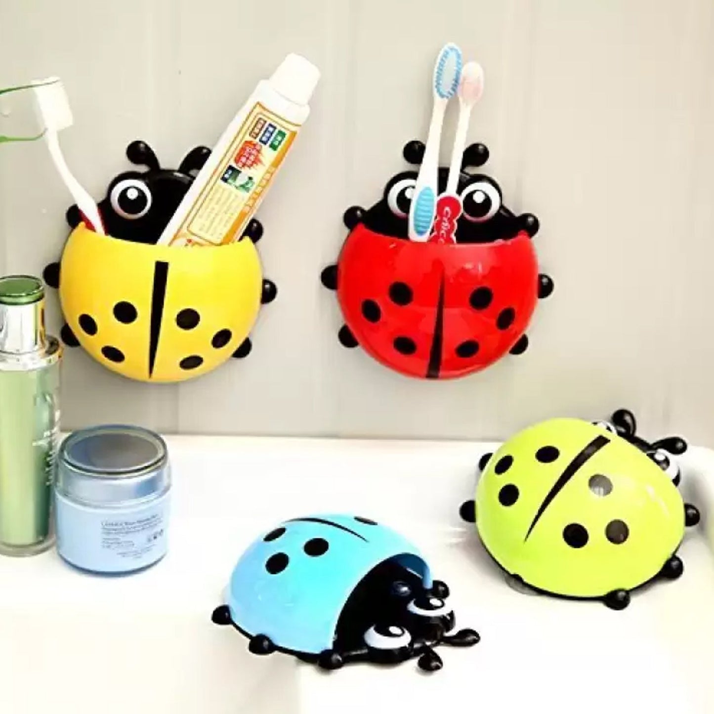 Four ladybug holders in yellow, red, blue, and green are displayed on a bathroom counter with toiletries.
