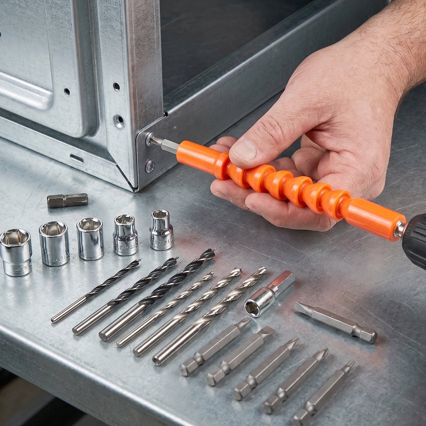 A hand uses an orange flexible bit extension with a drill to fasten a screw into a metal frame, surrounded by various bits.