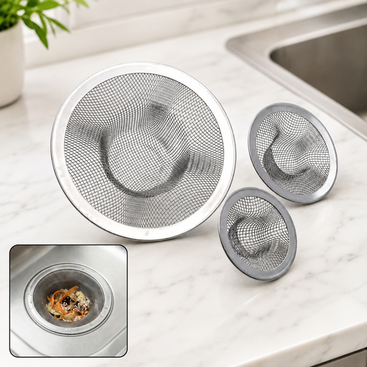 Three stainless steel mesh sink strainers of varying sizes on a white marble countertop next to a sink.