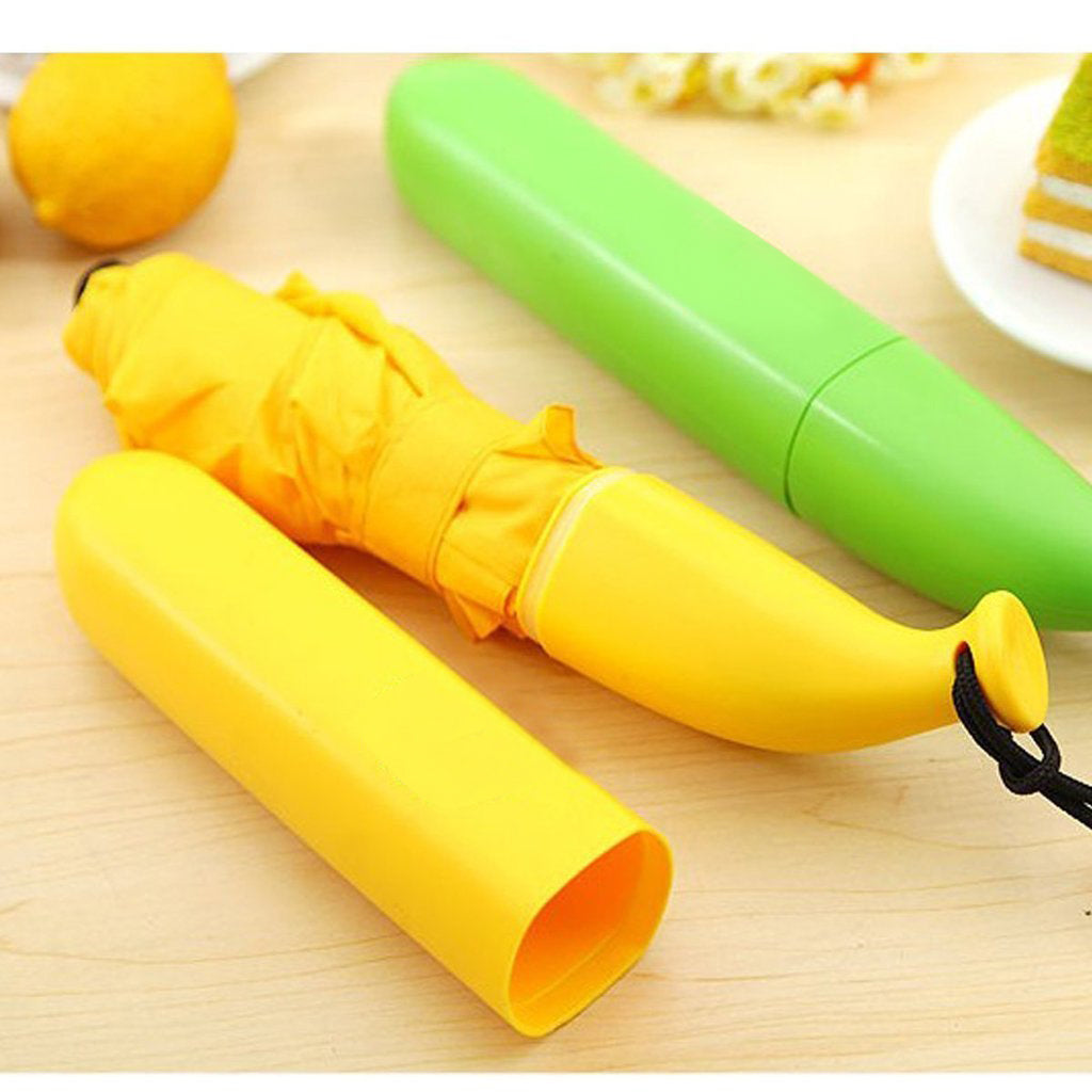 A yellow folded umbrella is partially inserted into its banana-shaped case, with a green case nearby on a wooden surface.