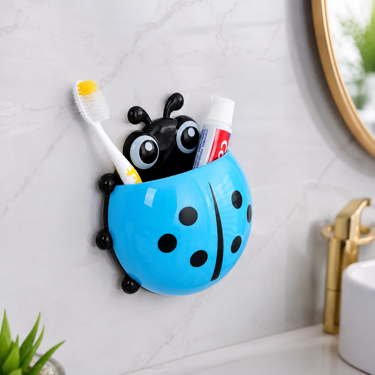 A blue ladybug holder with a toothbrush and toothpaste tube is suctioned to a white bathroom wall next to a sink.