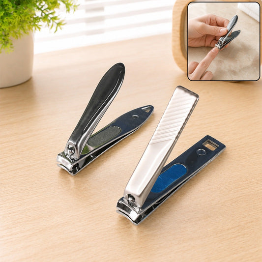 Two stainless steel nail clippers, one dark grey and one silver, on a wooden table with a plant.