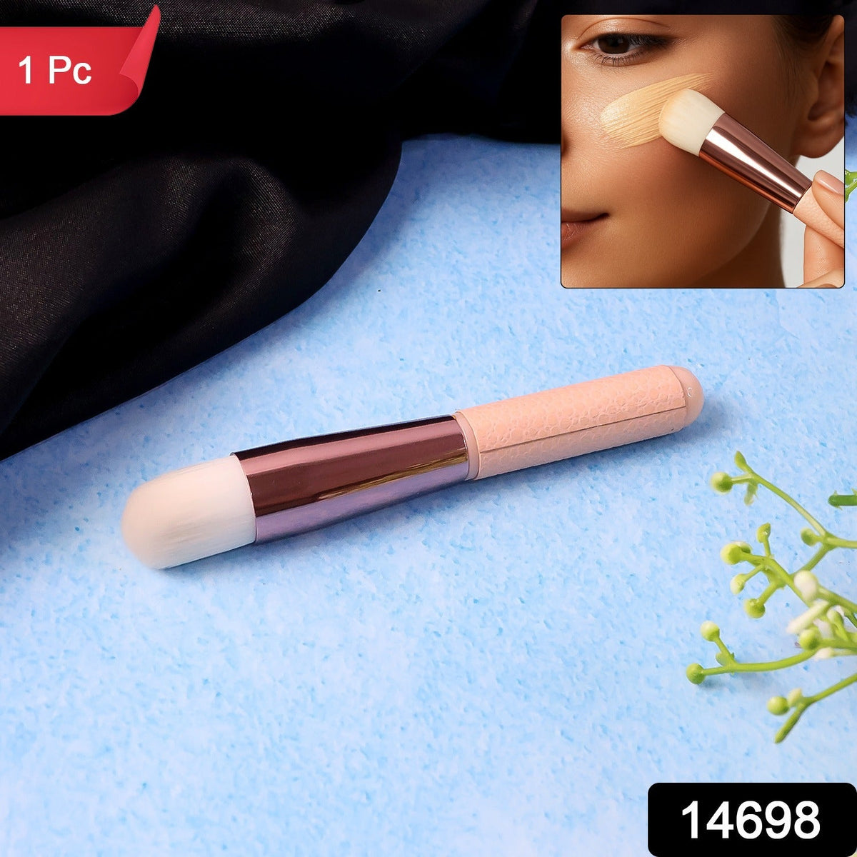 A pink and rose gold makeup brush on a blue textured surface with a black fabric and green leaves