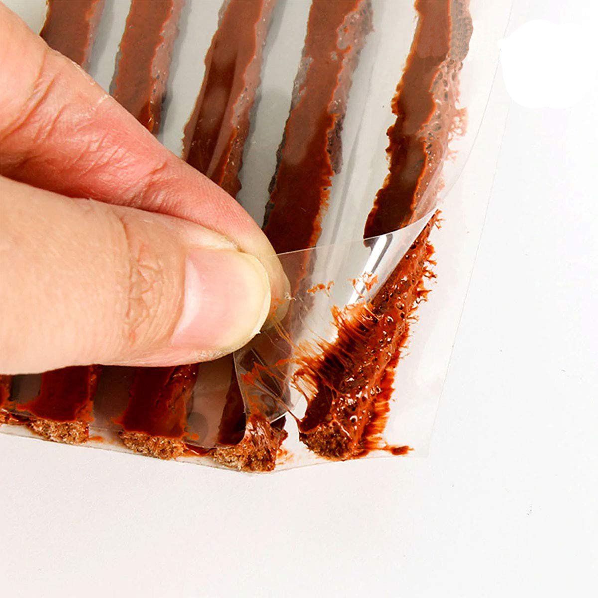 A hand peeling back the plastic from brown tire repair strips, revealing their sticky texture.