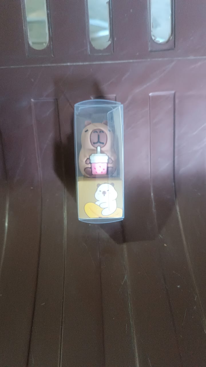 A capybara pencil sharpener in clear packaging with a graphic of a white capybara, on a brown ribbed surface.