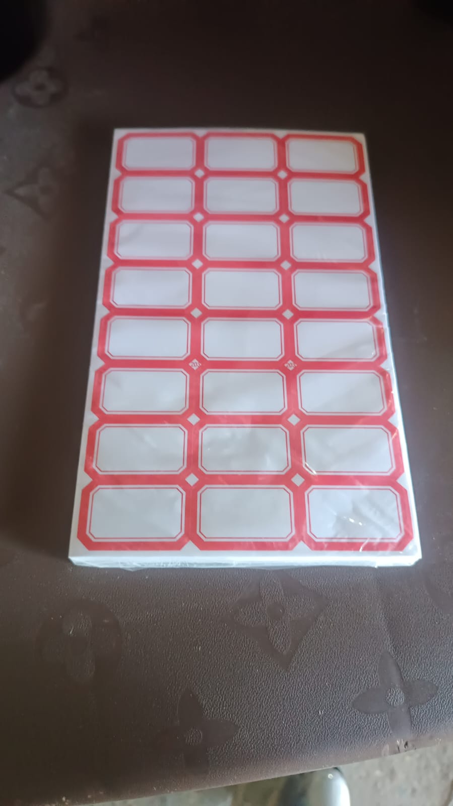 A stack of white labels with red borders, wrapped in plastic, on a dark brown surface.