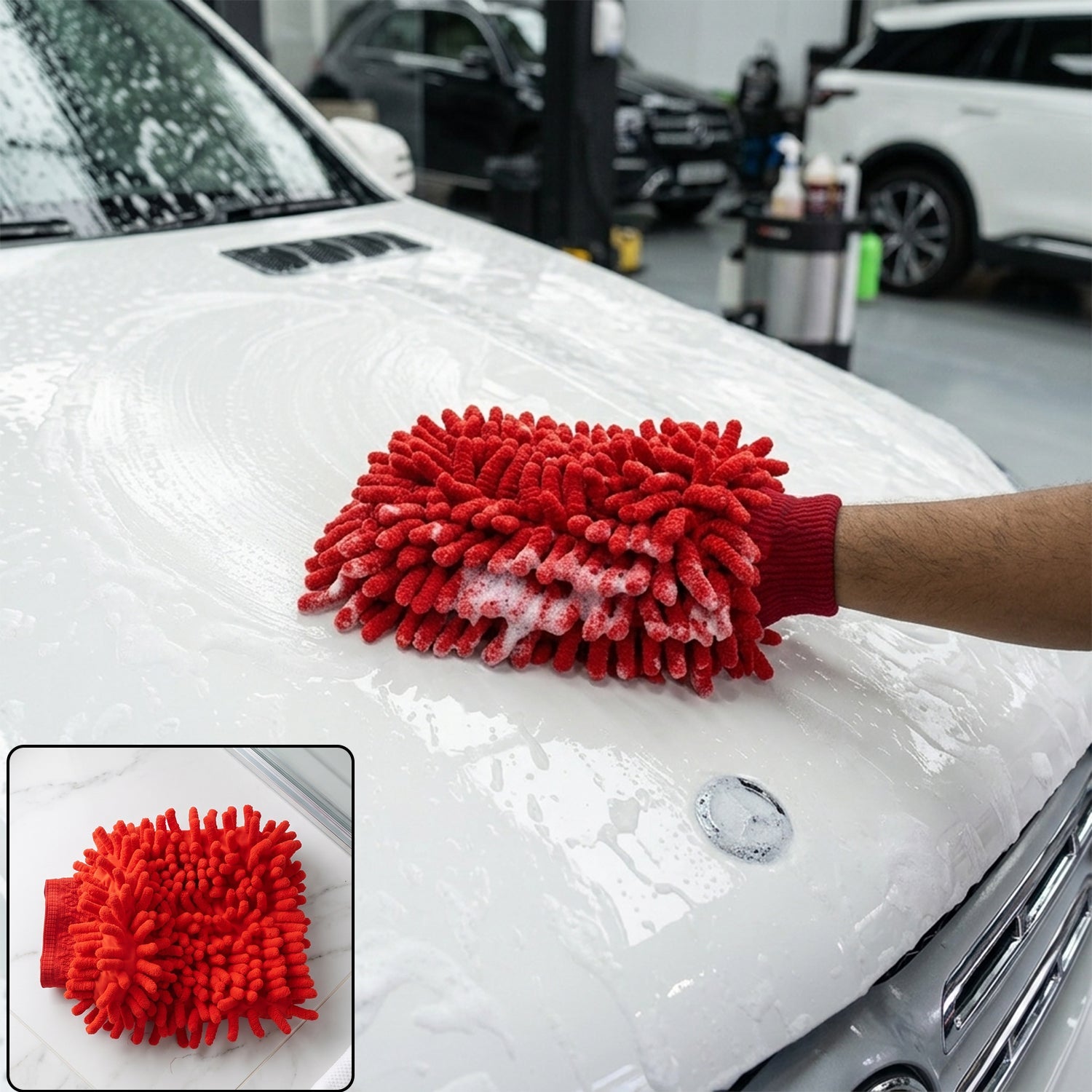 A person's gloved hand uses a red chenille microfiber car wash glove to clean a white car's hood, covered in suds.