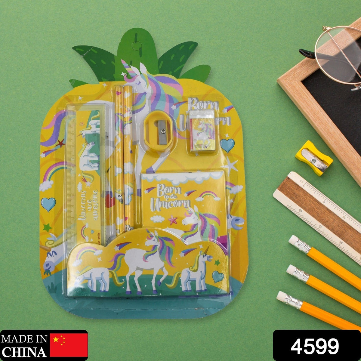 A yellow unicorn stationery set in pineapple packaging on a green background, with a small chalkboard and pencils nearby.