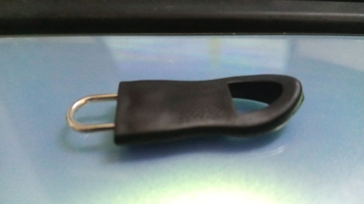 A black rubber zipper pull tab with a silver metal loop is placed on a shiny blue-grey surface.