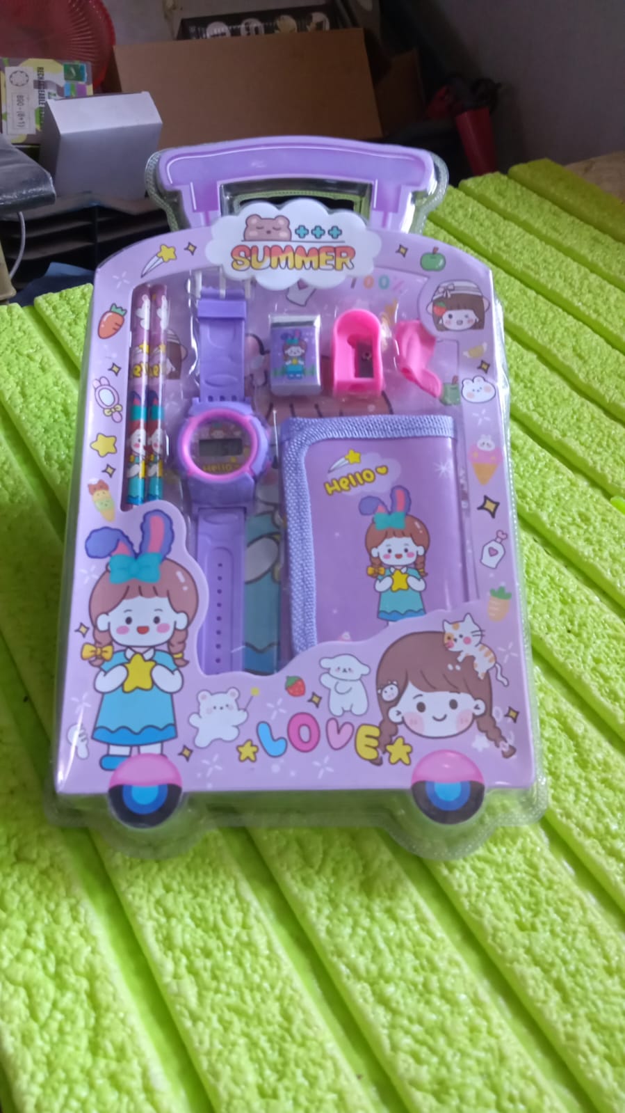 A purple stationery set in a trolley-shaped package, including a watch, pencils, eraser, sharpener, and wallet, resting on a
