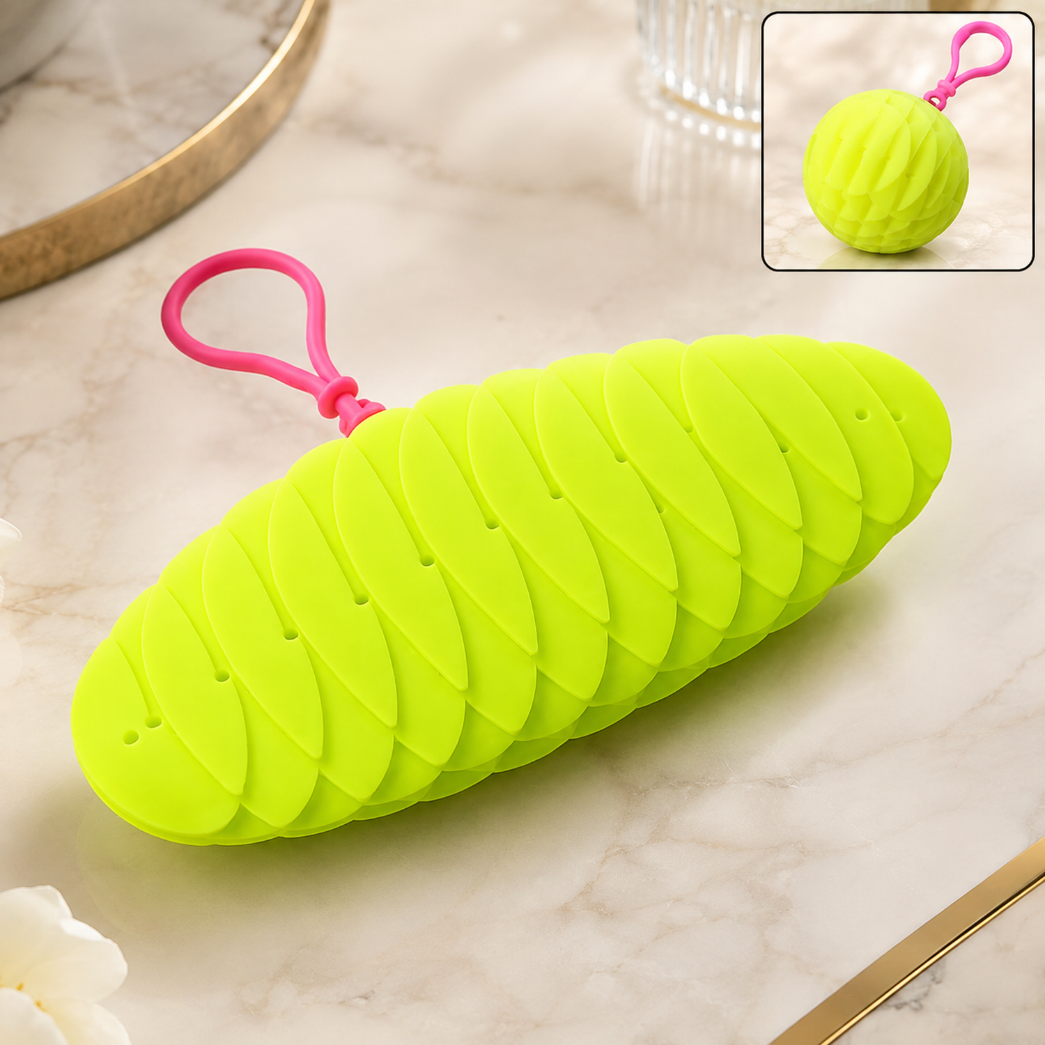 A bright green collapsible silicone ball keychain with a pink loop, shown partially collapsed on a marble surface