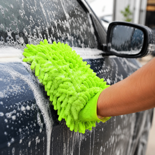 A hand in a bright green microfiber glove washes a dark blue car, covered in white soap suds.