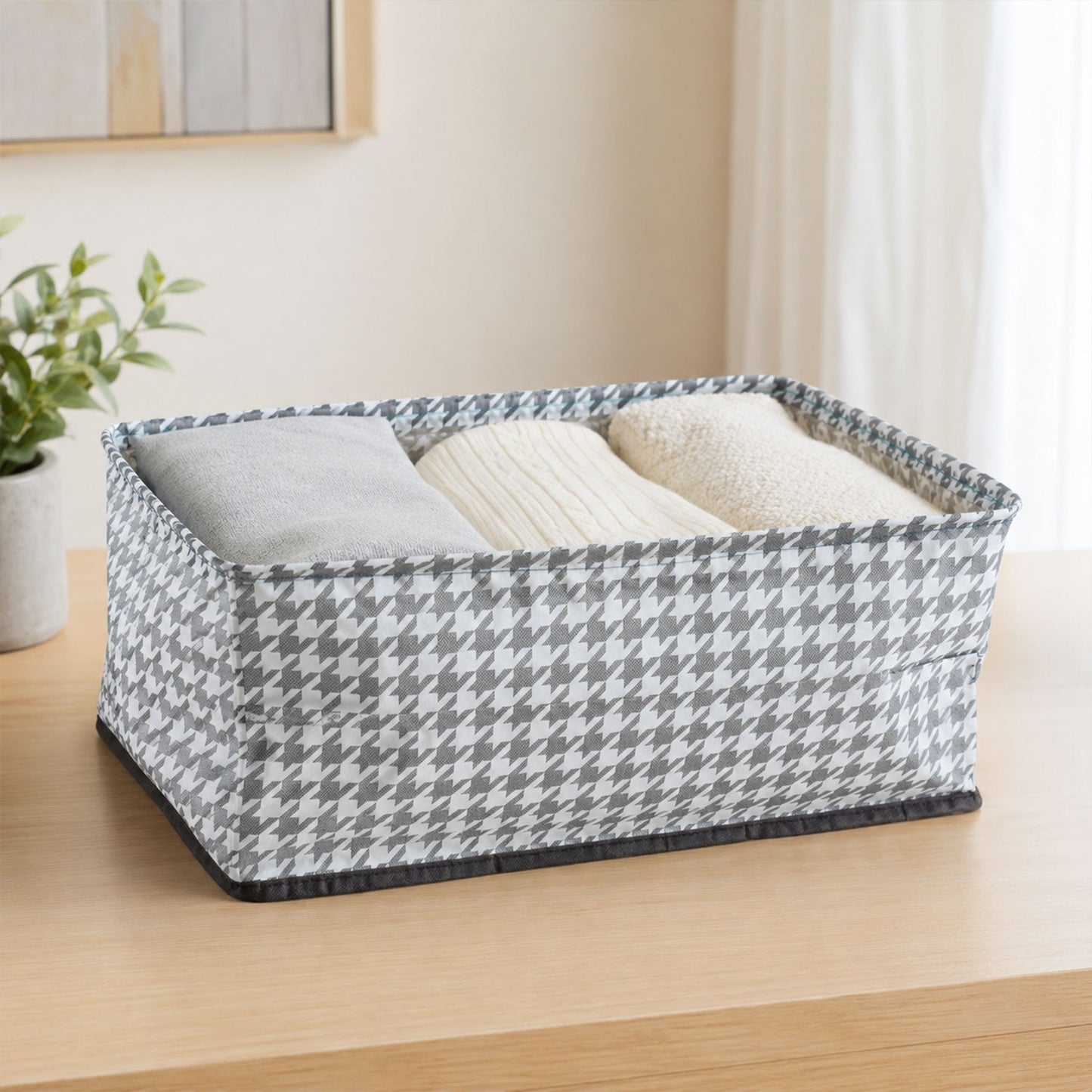 A gray and white houndstooth fabric basket is filled with folded gray and white clothing on a wooden table.
