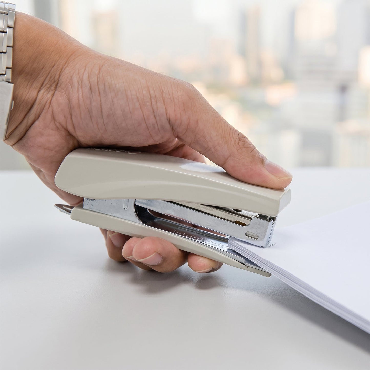 A person's hand presses down on a beige and silver stapler, securing a stack of white papers.