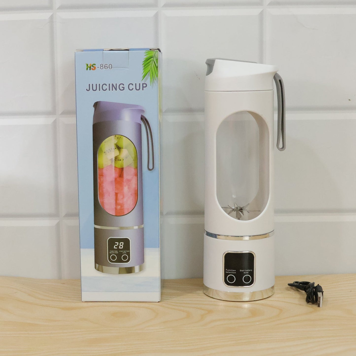 A white portable blender with a clear window and blades next to its product box on a wooden surface.