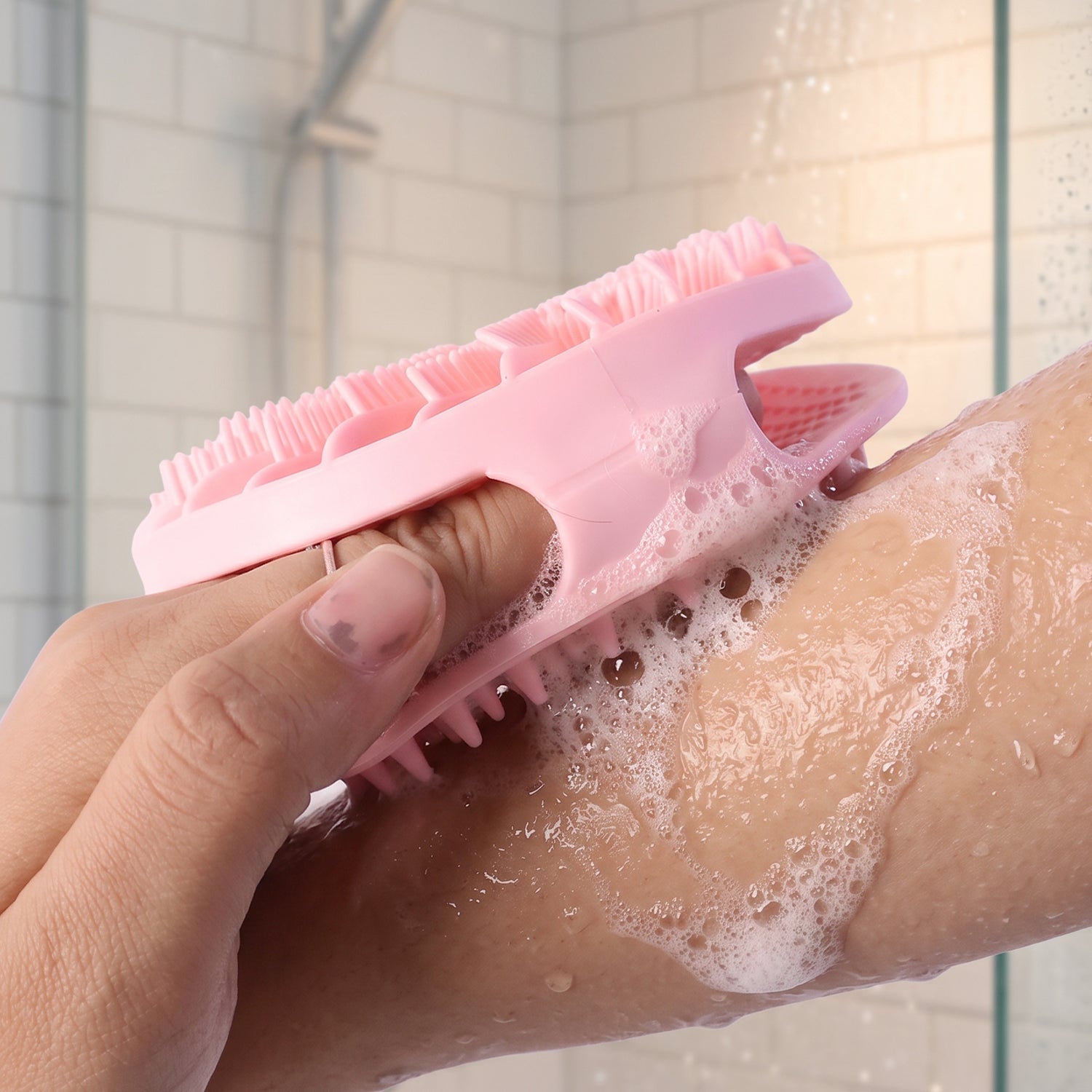 A hand holds a pink silicone body scrubber, lathering soap on an arm in a shower with a small inset image and a '22899'