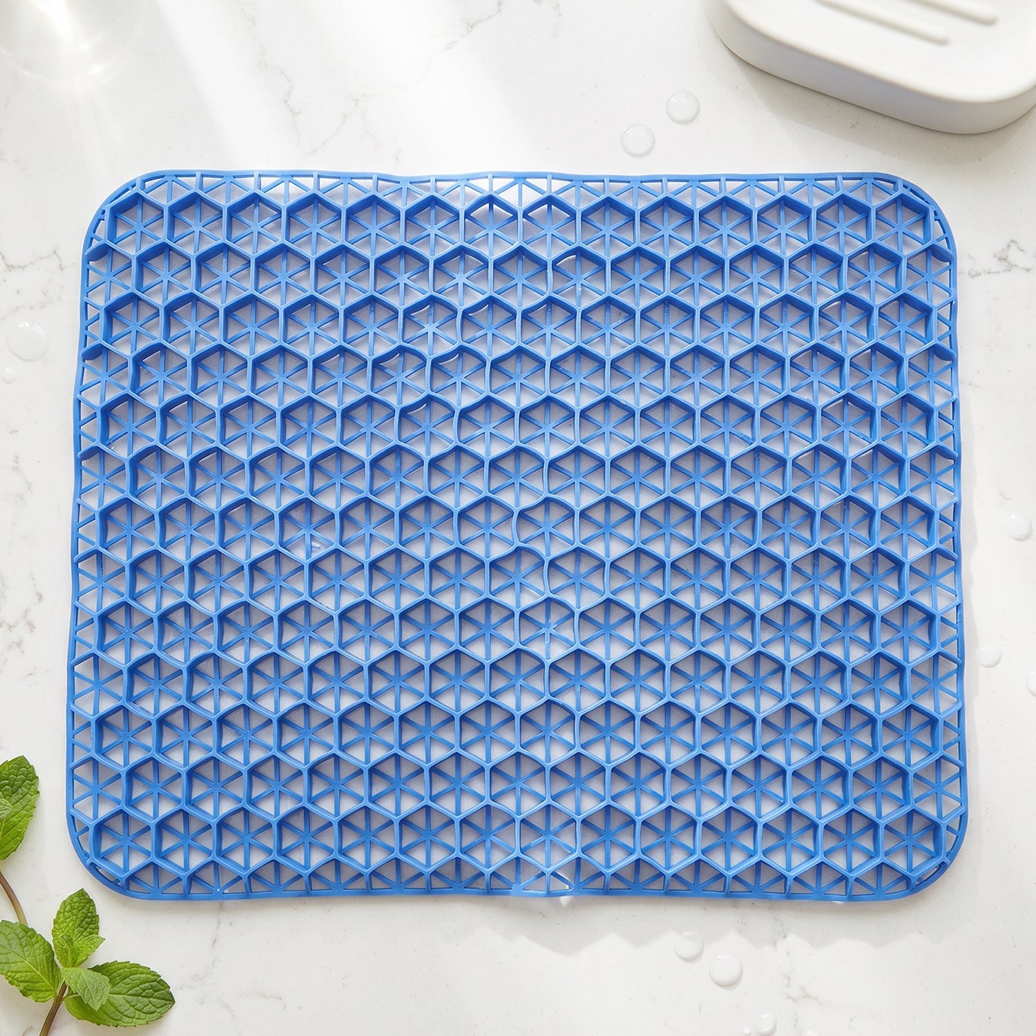 Close-up, top-down view of the blue honeycomb gel cushion on a white surface with a mint sprig.