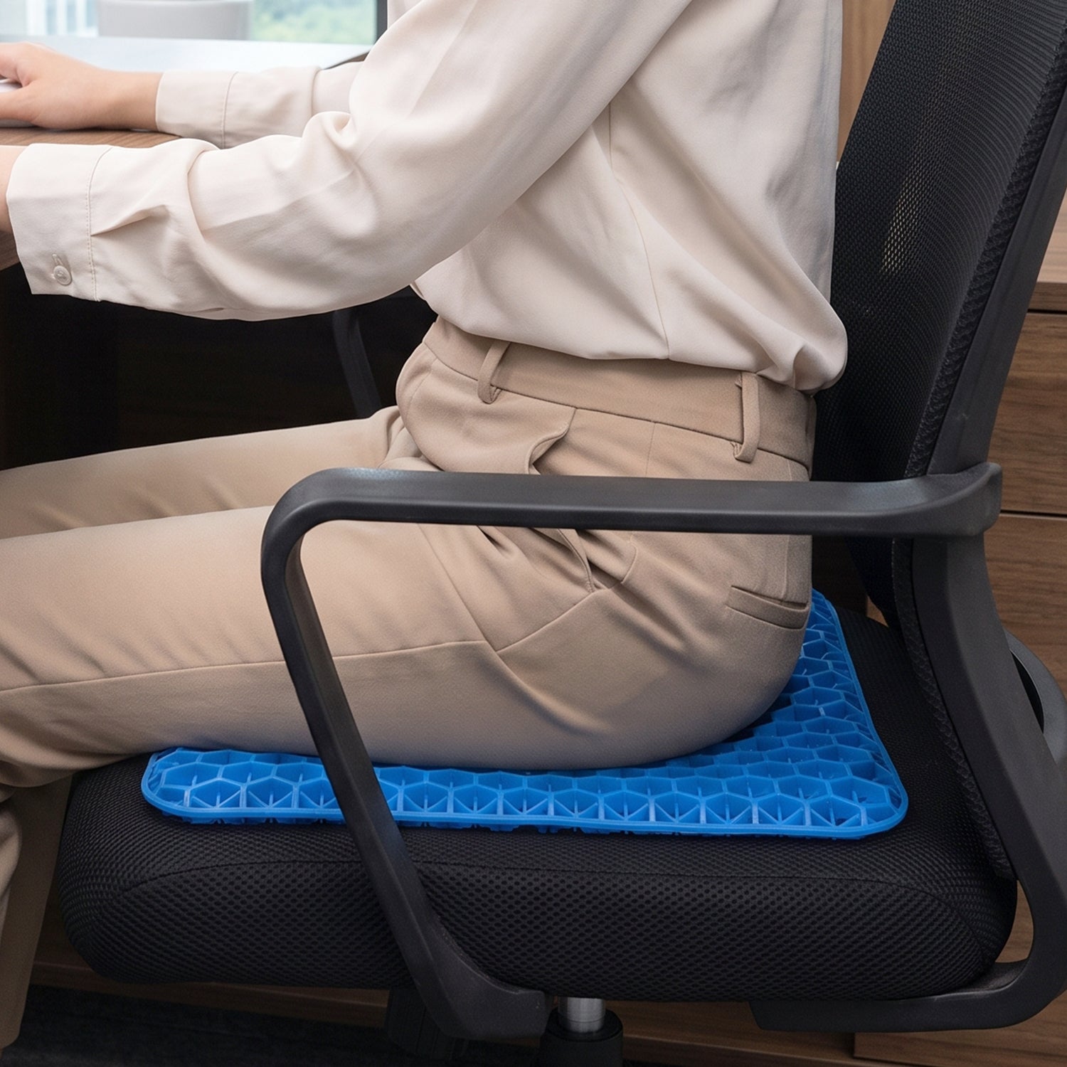 Person in beige pants and shirt sitting on an office chair with the blue honeycomb gel cushion.