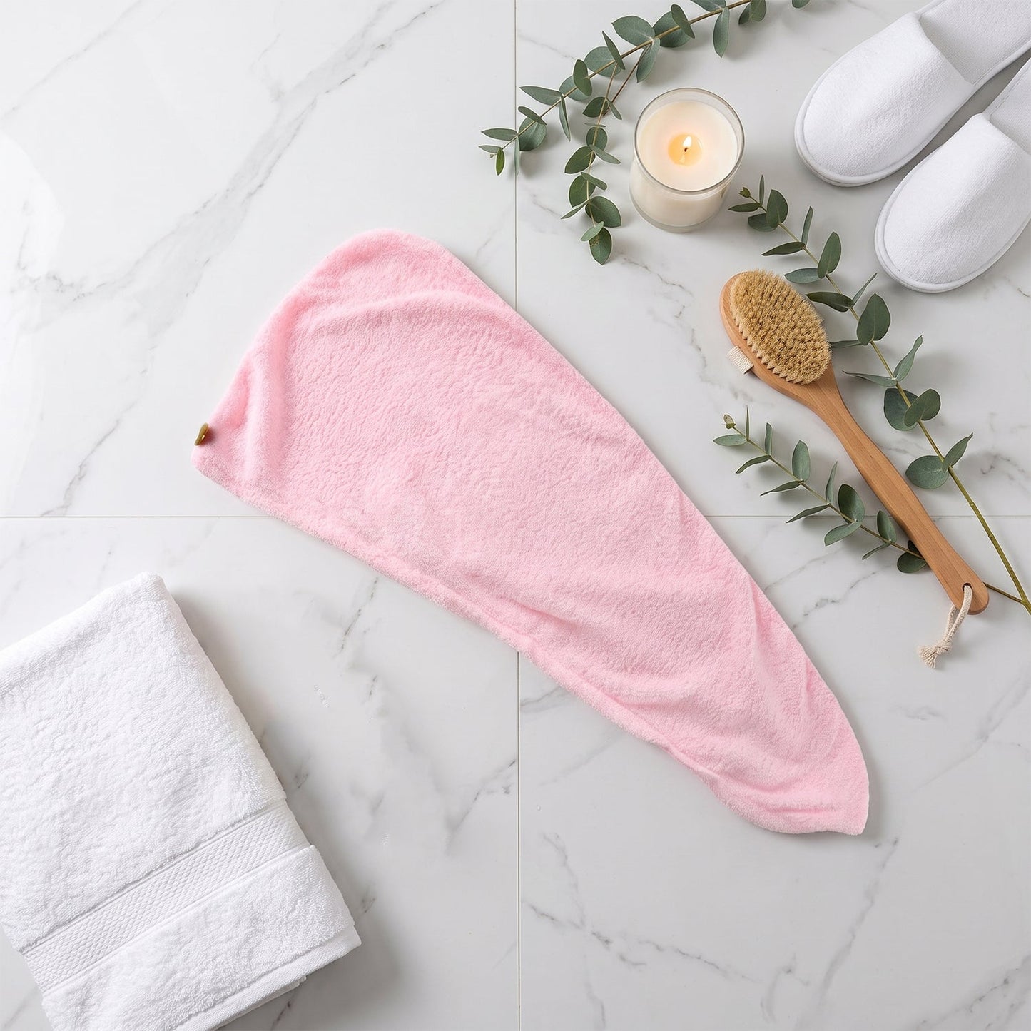 A pink microfiber hair wrap lies flat on a white marble surface, next to a white towel and brush.