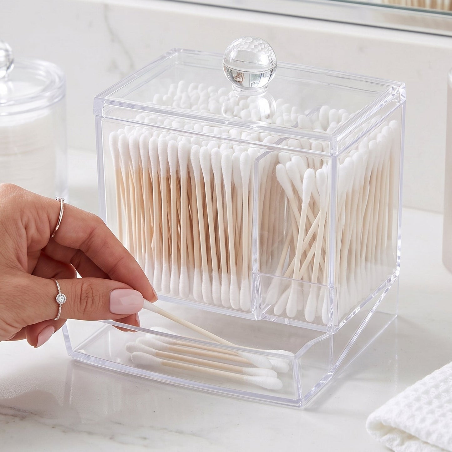 A hand taking cotton swabs from the dispensing drawer of a clear acrylic organizer.