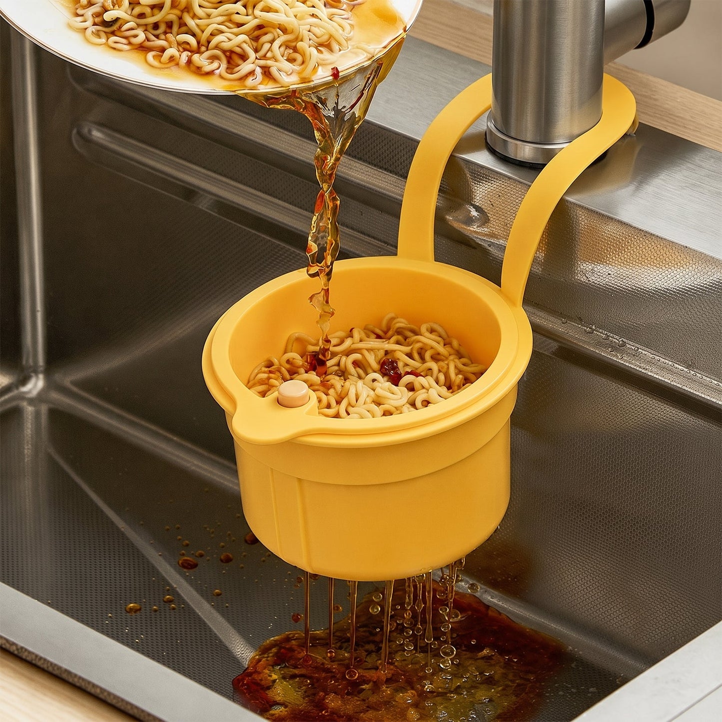 A yellow plastic hanging kitchen sink drain basket and food strainer with handle drains noodles into a stainless steel sink.