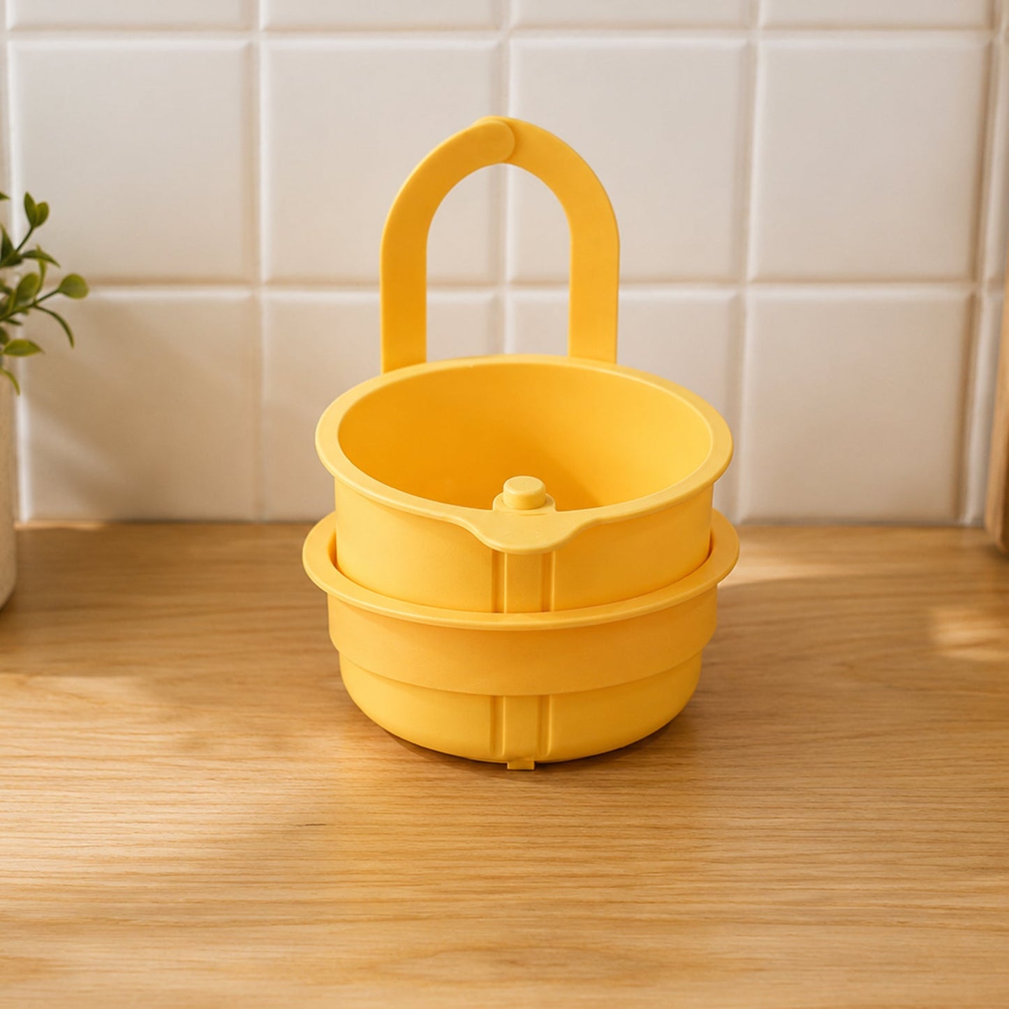 A yellow plastic hanging kitchen sink drain basket and food strainer with handle sits on a light wood surface.