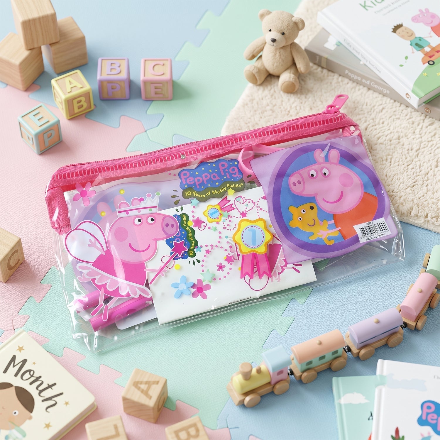 A clear pink-zippered pouch with the Peppa Pig stationery set, surrounded by children's toys on a playmat.