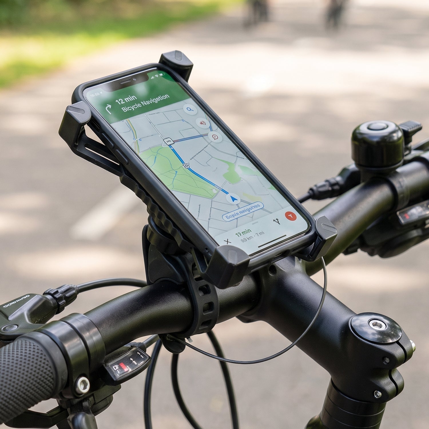 A black phone holder with a phone displaying a map is mounted on bicycle handlebars, with a small horn shown in the corner.