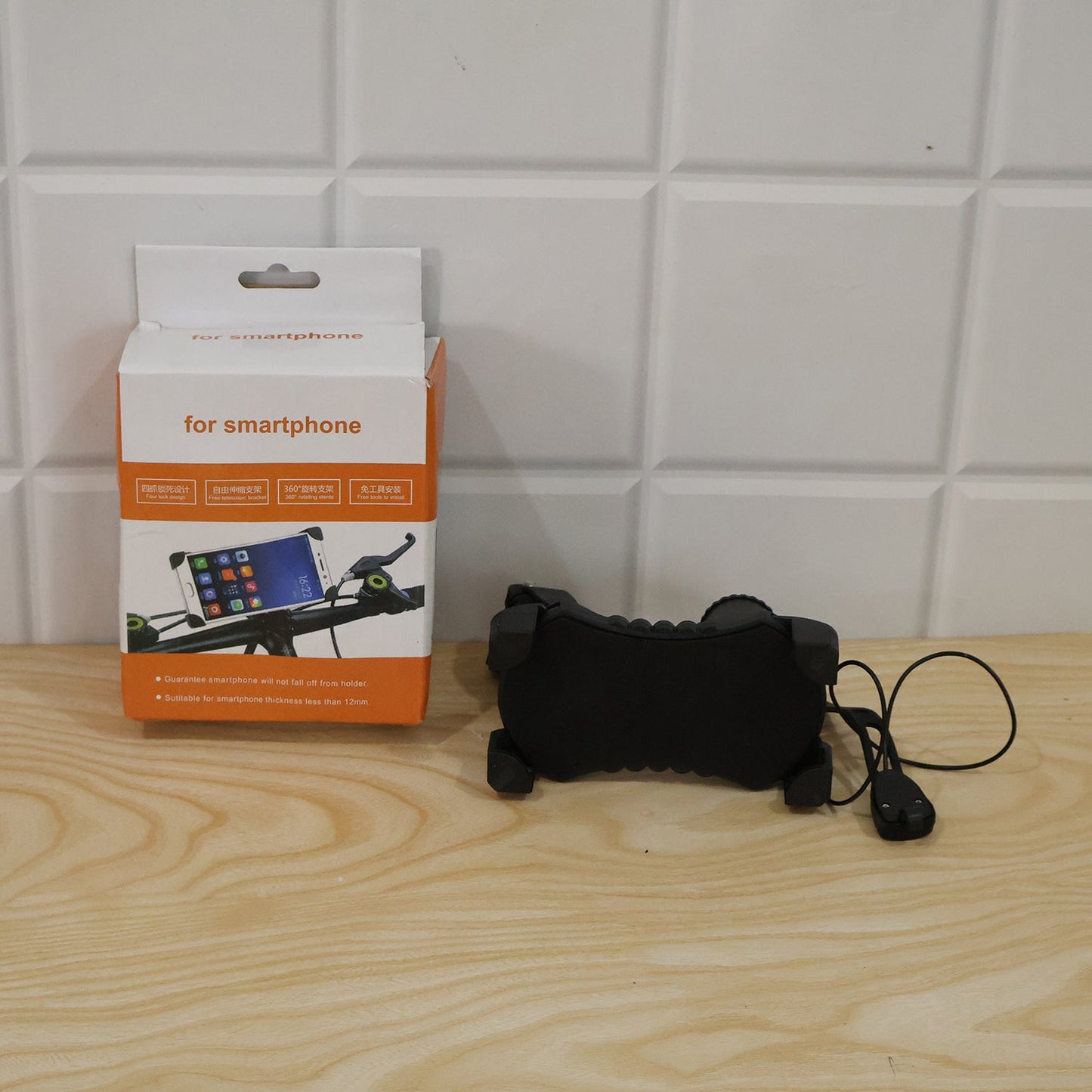 A black bicycle phone holder with a horn and its orange and white packaging box are on a wooden surface.