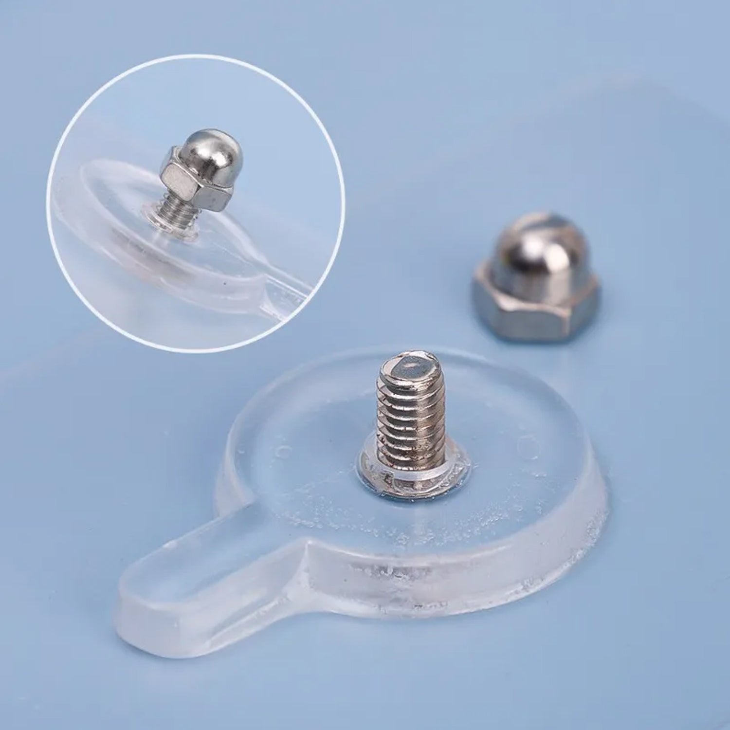 A disassembled clear self-adhesive wall hook shows the threaded silver bolt and separate silver cap on a blue surface.