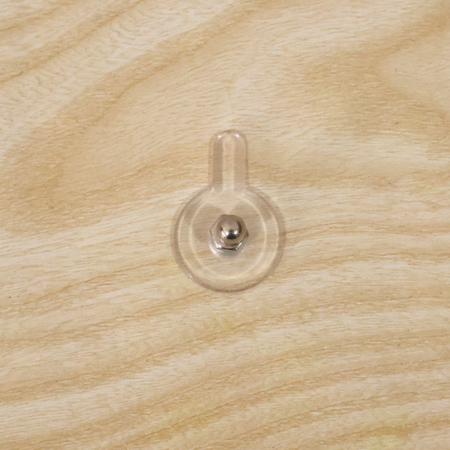 A clear self-adhesive wall hook with a silver knob is attached to a light-colored wooden surface.