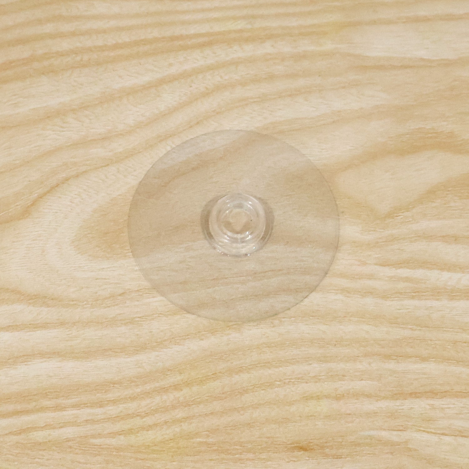 A clear plastic suction cup hook is centered on a light brown wooden surface with visible grain.