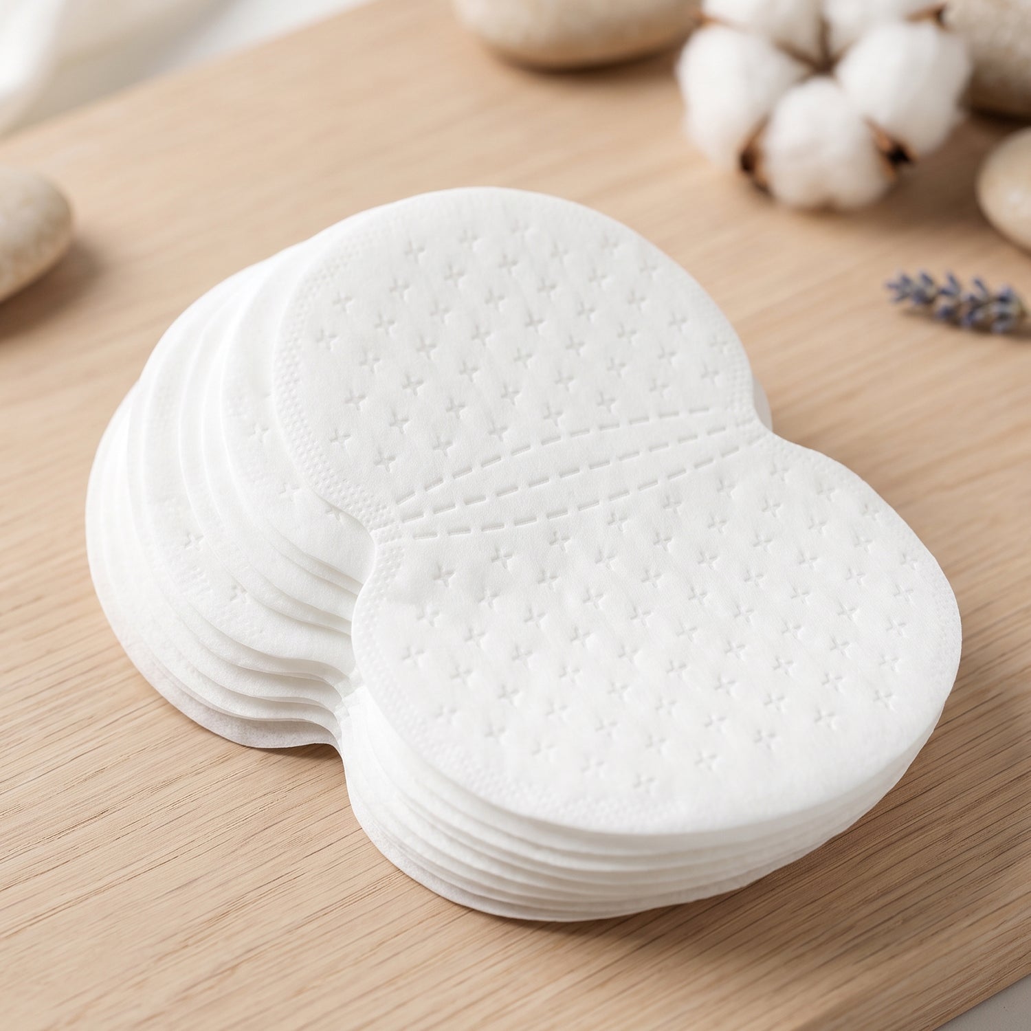 A stack of white, disposable underarm sweat pads with a textured surface on a wooden surface.