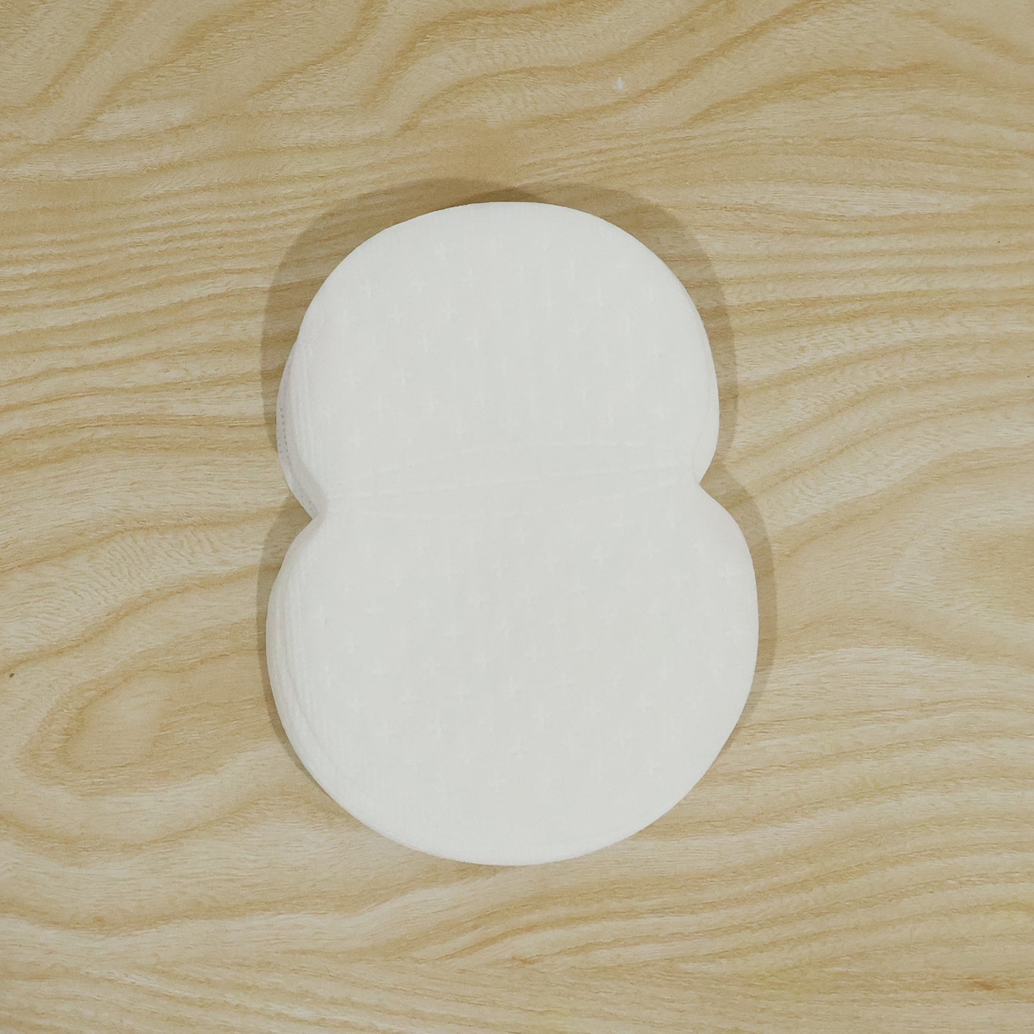 A stack of white, disposable underarm sweat pads with a smooth surface on a wooden background.