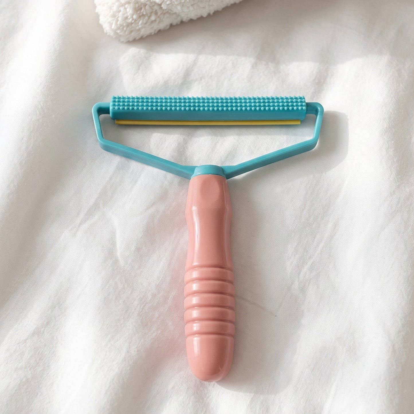 A pink and blue lint remover with a textured handle rests on a white textured fabric surface.