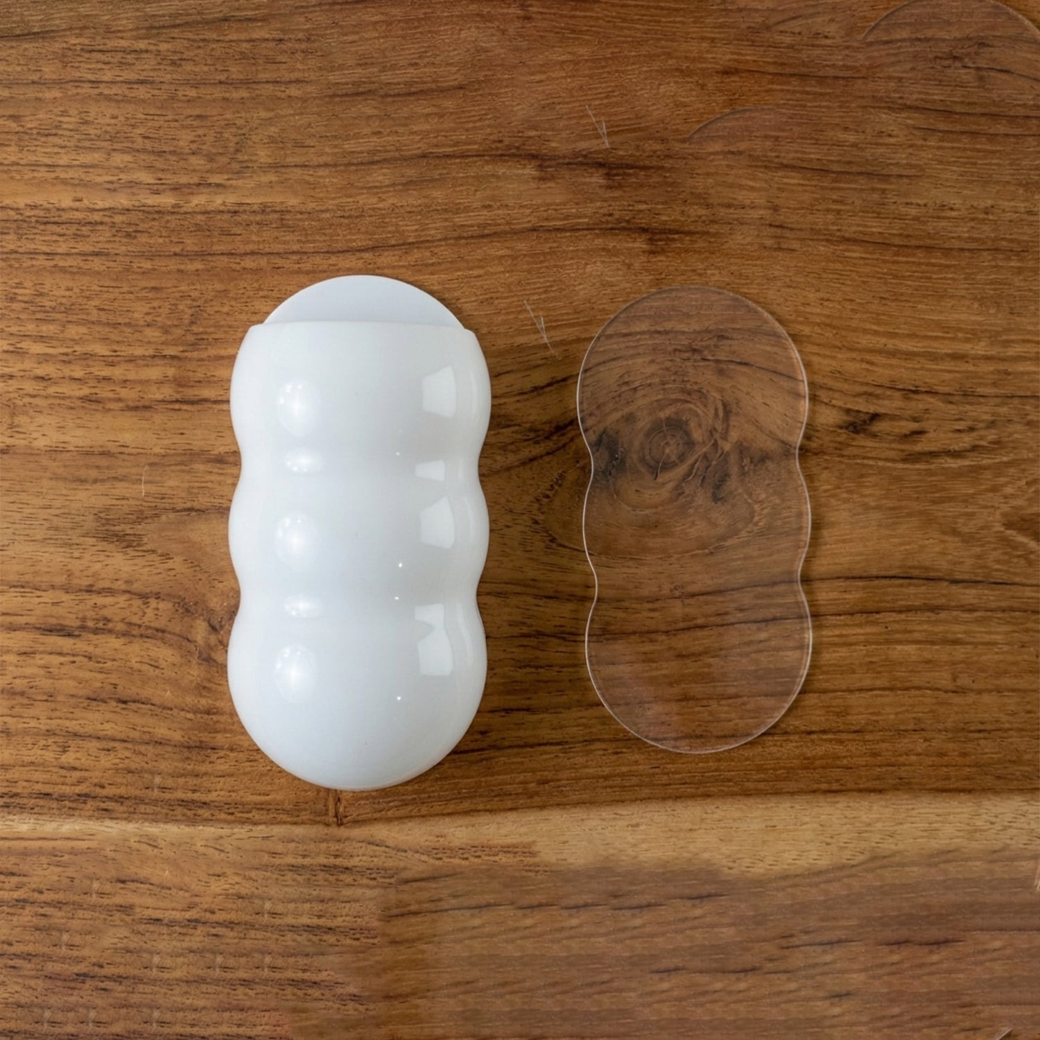 White, caterpillar-shaped holder and a clear adhesive strip on a light brown wooden surface.
