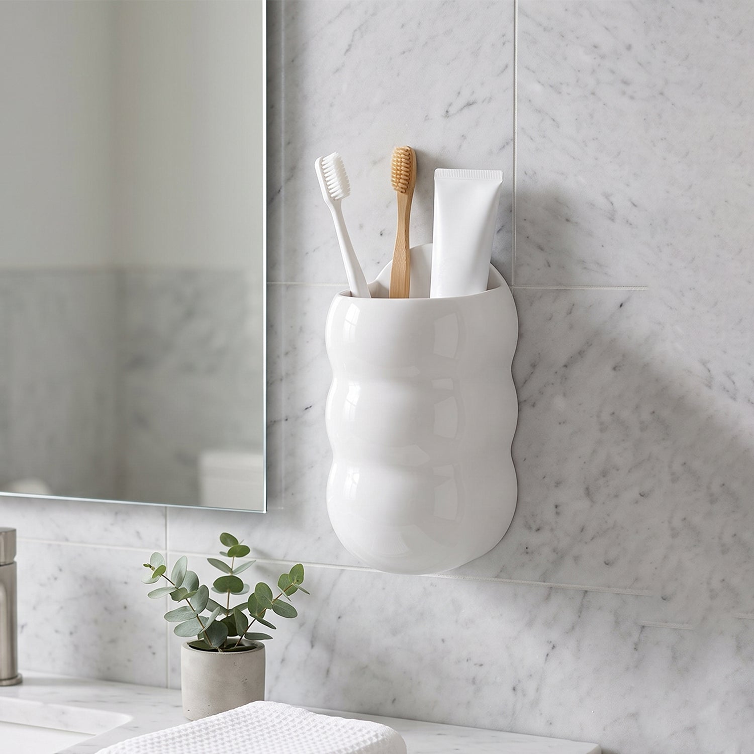 White, caterpillar-shaped wall holder with toothbrushes and toothpaste in a bathroom with a plant and mirror.