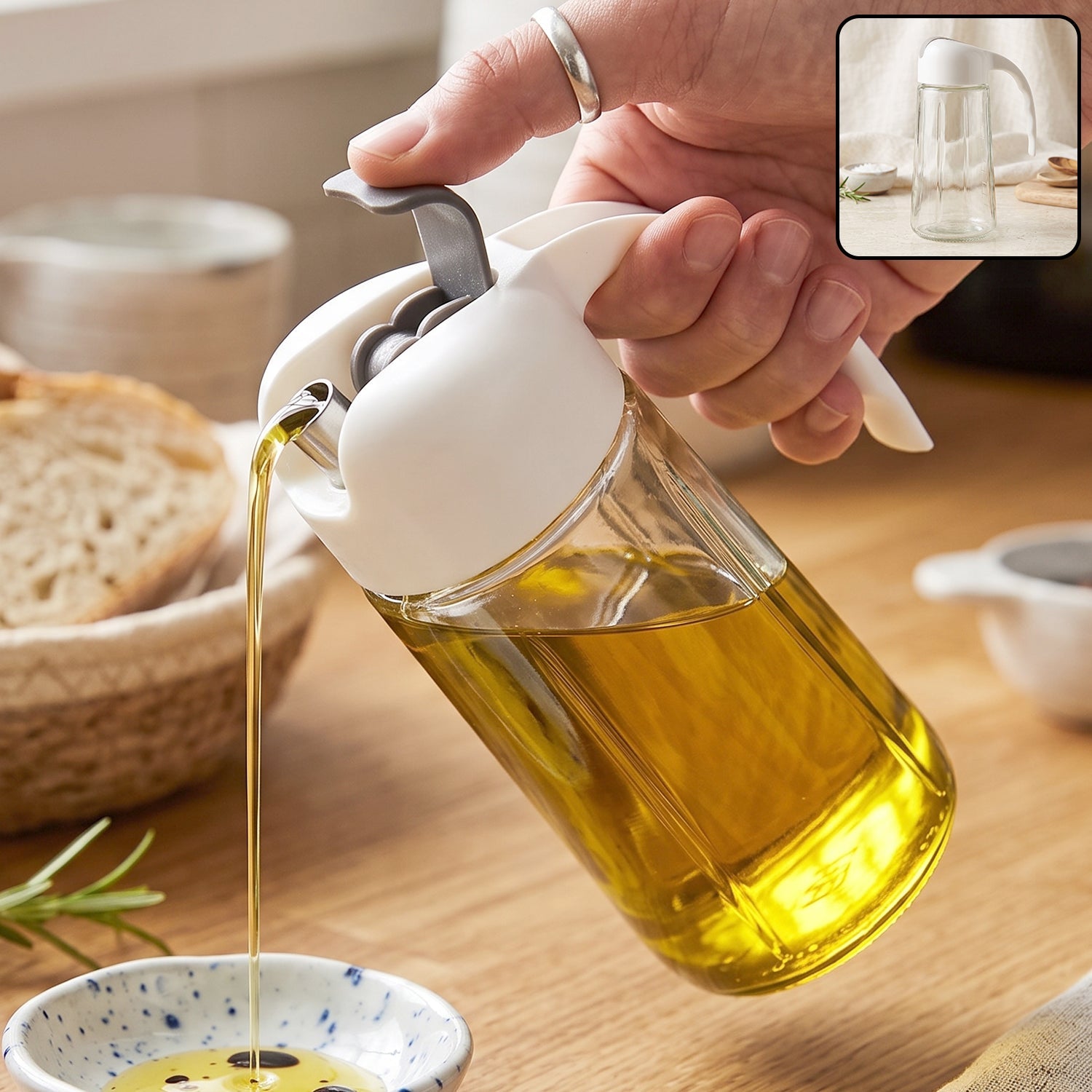 A hand holds a clear glass oil dispenser with a white and gray lid, pouring golden oil into a small dish.