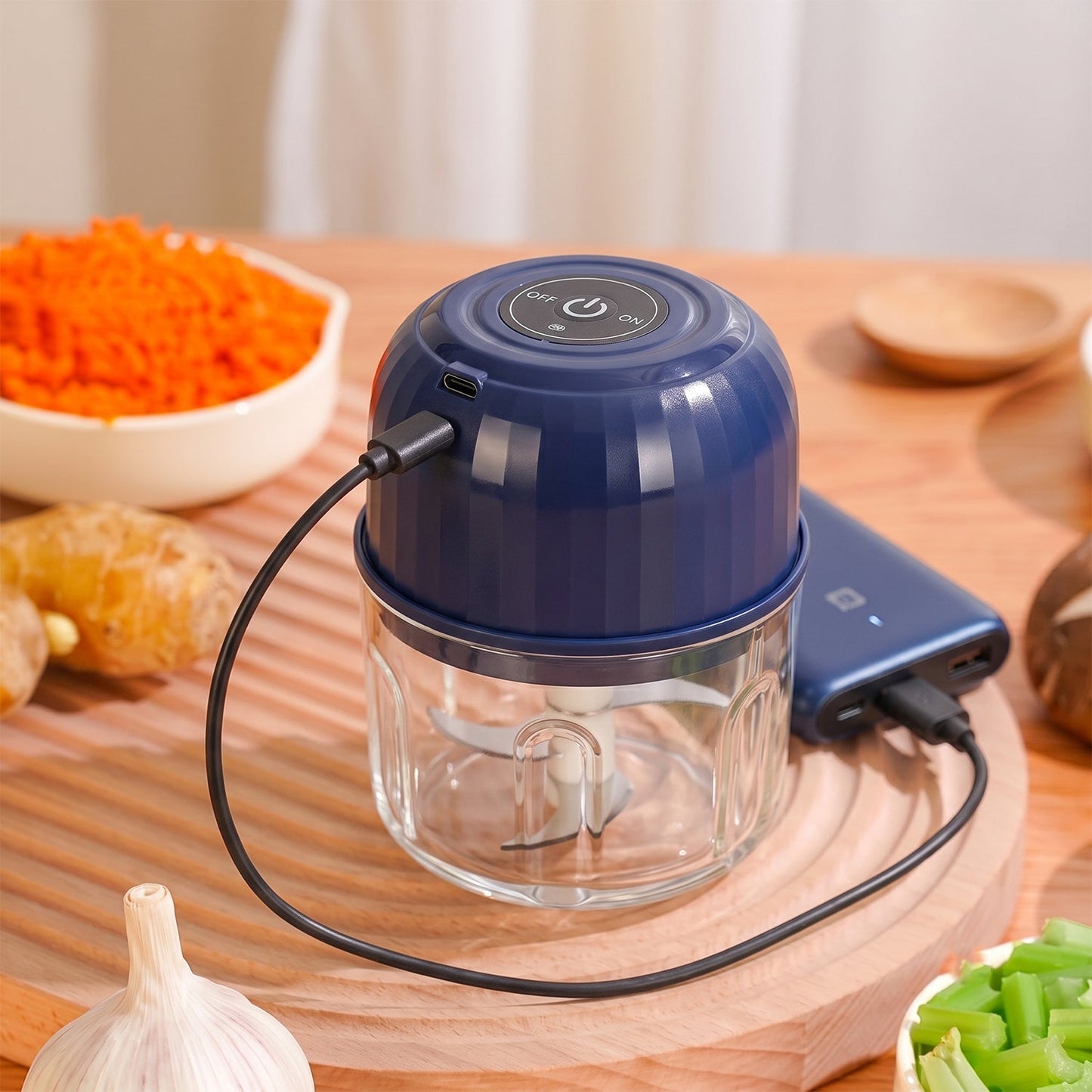 The dark blue mini food chopper, with a clear glass bowl, is shown connected to a power bank via a black USB cable.