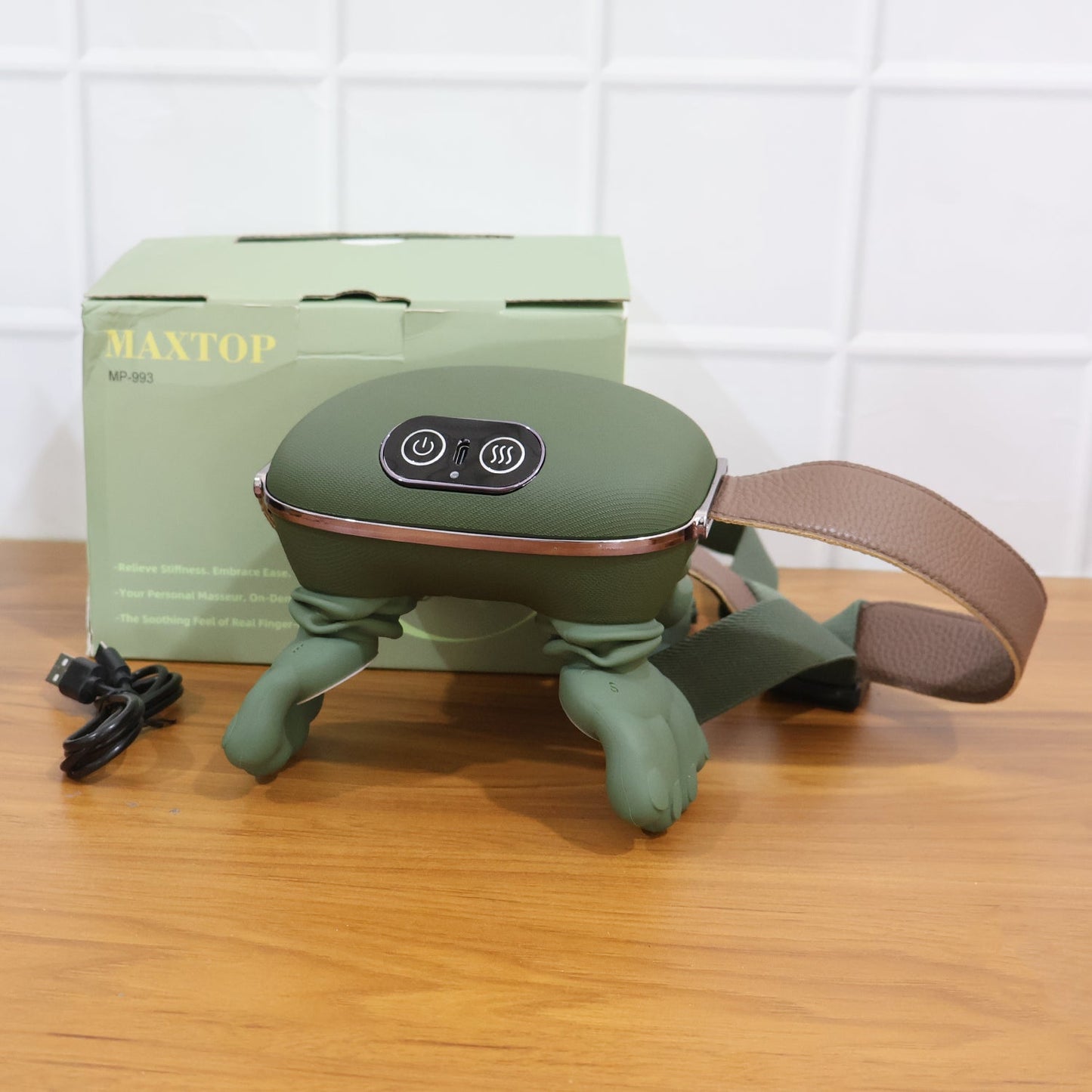 A green bionic massager with a brown strap and a black charging cable rests on a wooden surface next to its green product