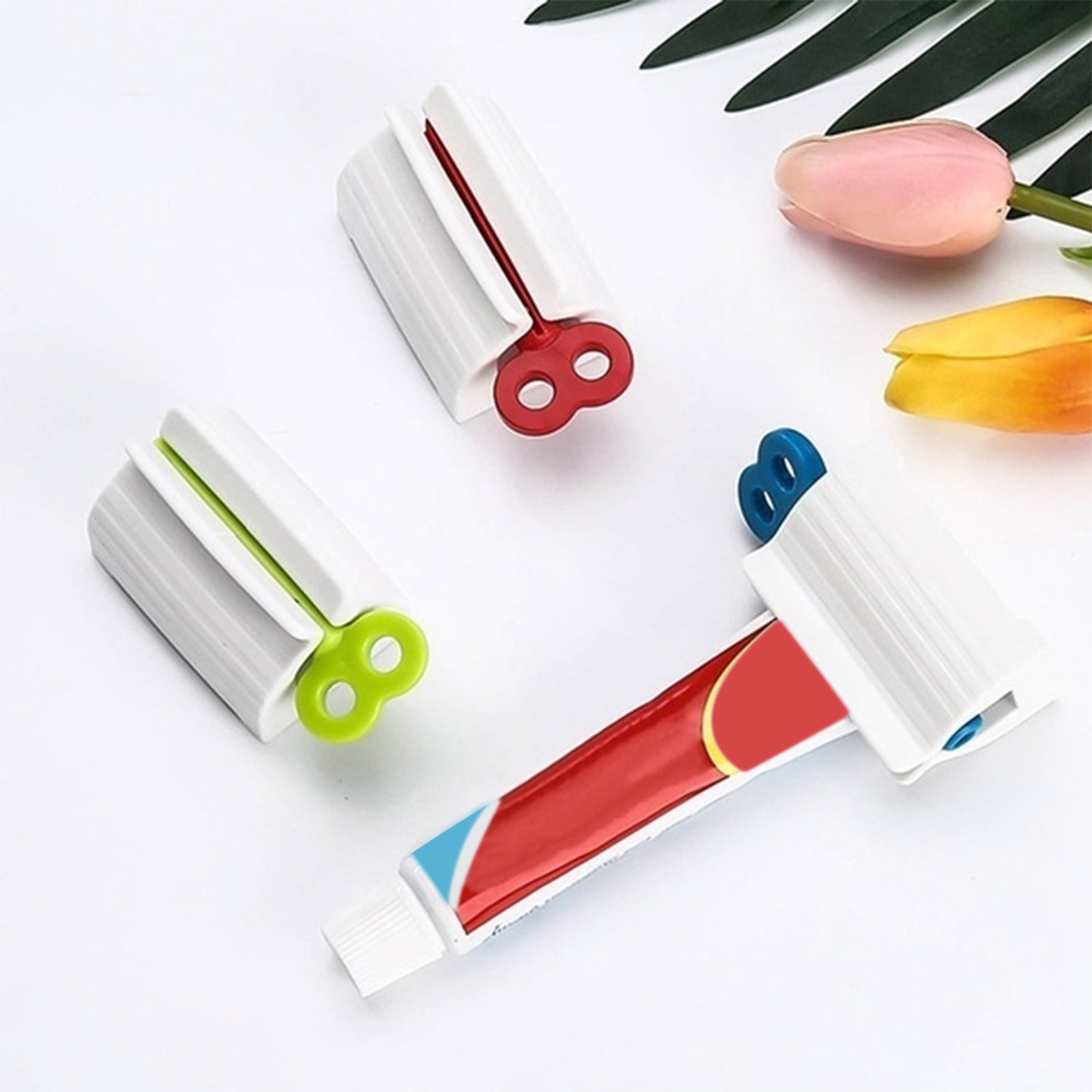 Three white tube squeezers with red, green, and blue winding keys are shown with a toothpaste tube on a white surface