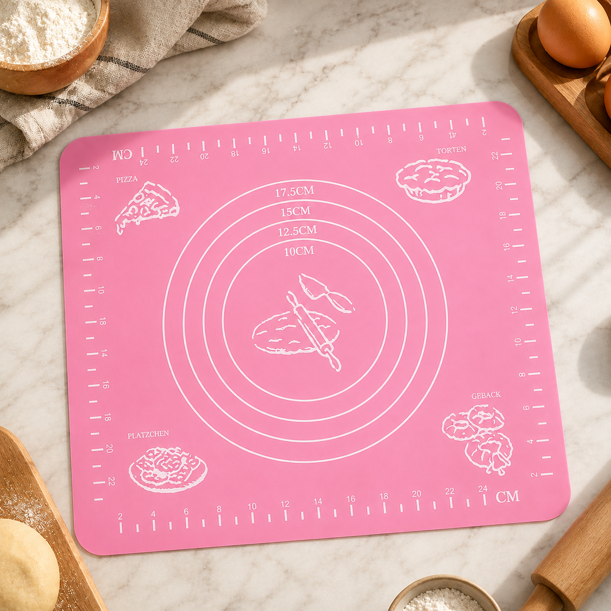 Pink silicone baking mat with white measurement guides and baking illustrations, surrounded by baking ingredients.
