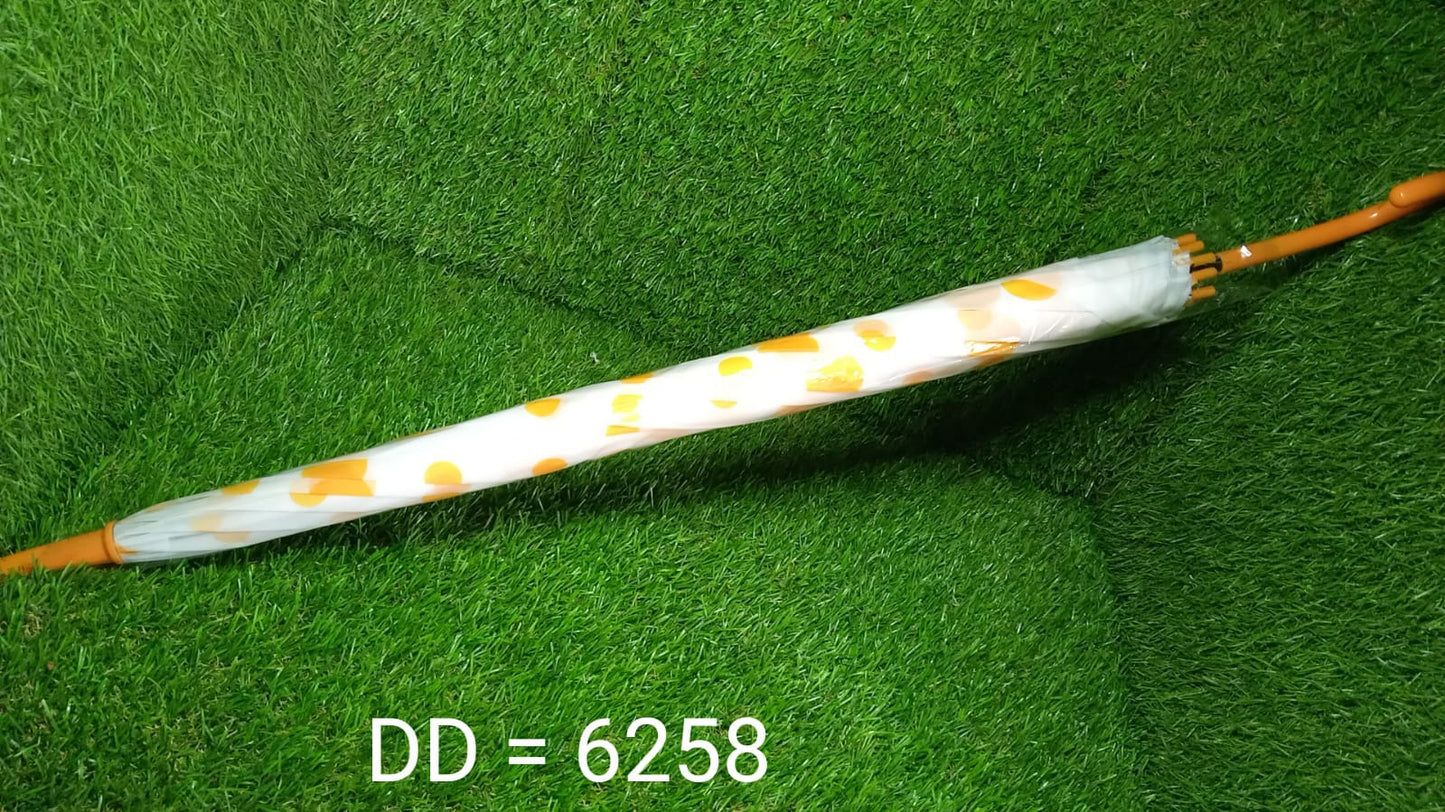 A closed white umbrella with yellow polka dots and a brown handle rests horizontally on a green artificial grass background.