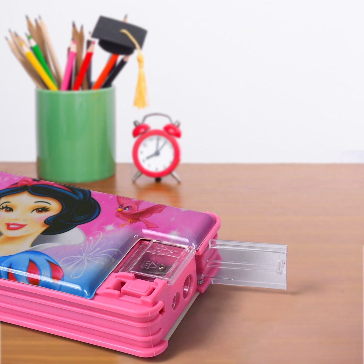 Close-up of a pink Disney princess pencil case with its sharpener tray extended, on a wooden desk.