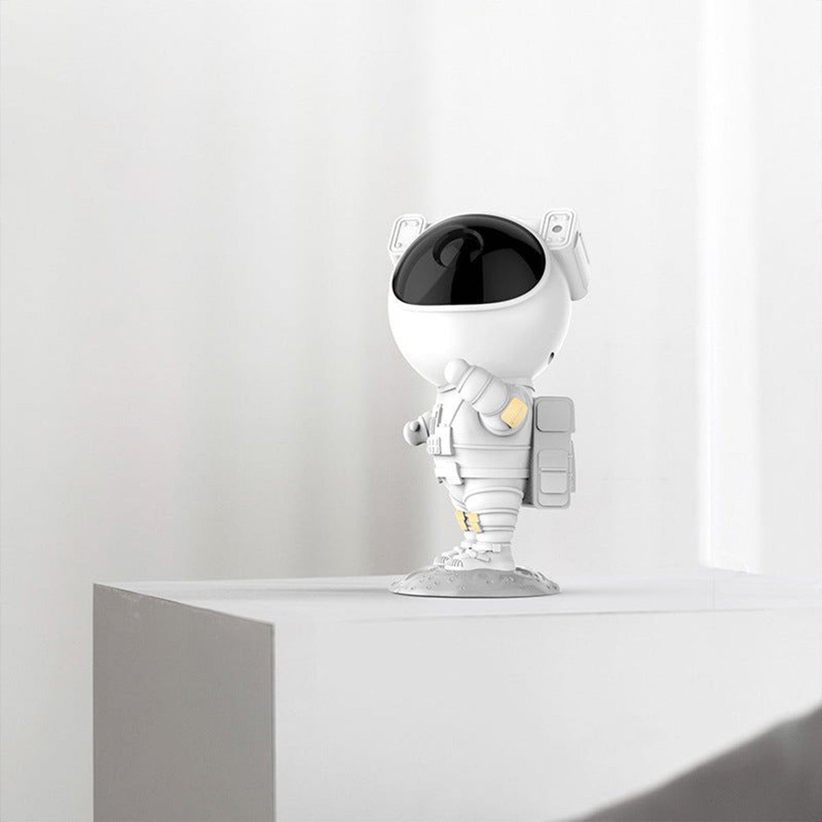 A white astronaut projector with a black visor stands on a white shelf against a plain white wall.