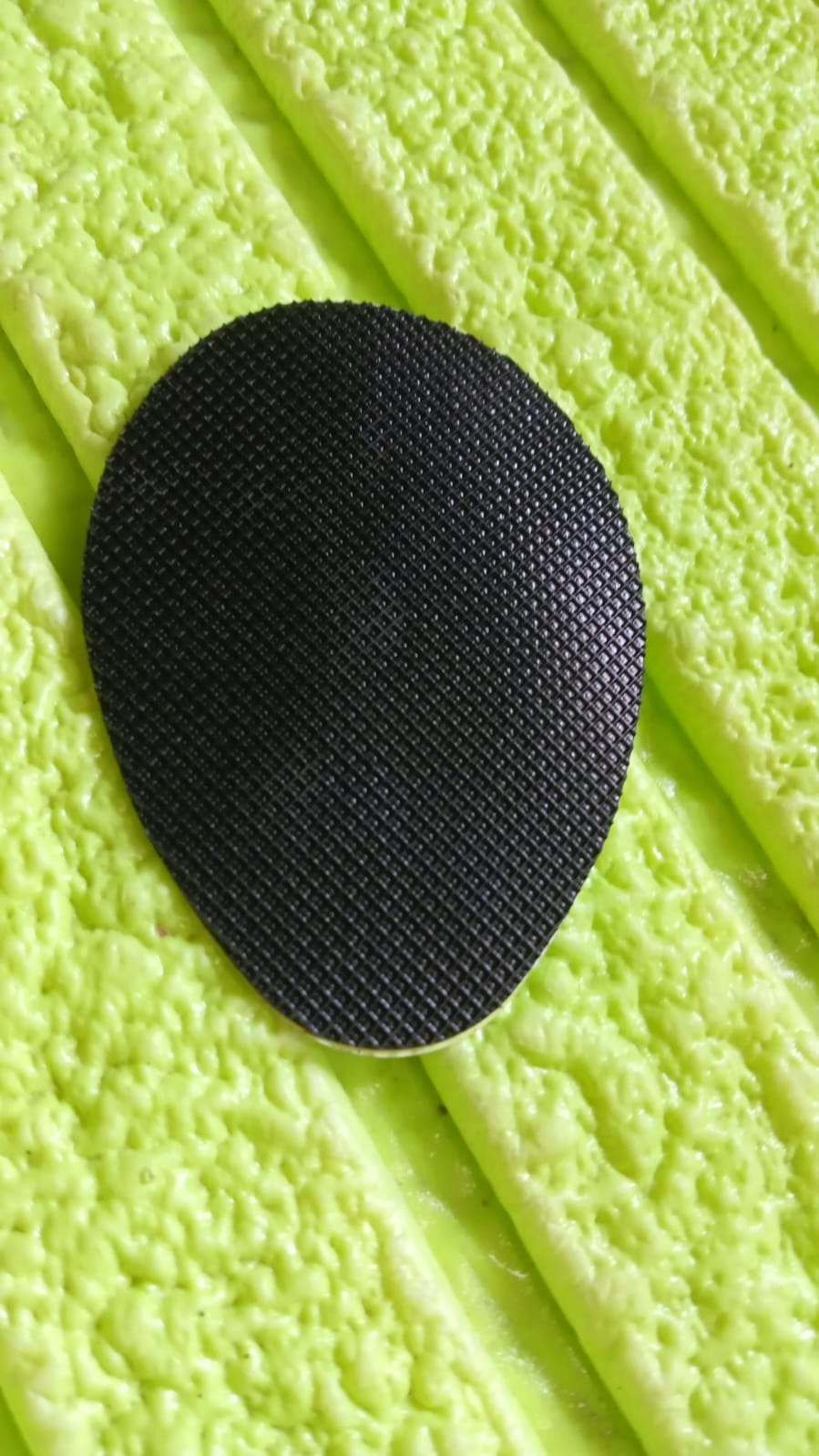 A single black non-slip shoe pad with a textured surface rests on a bright green, ridged background.