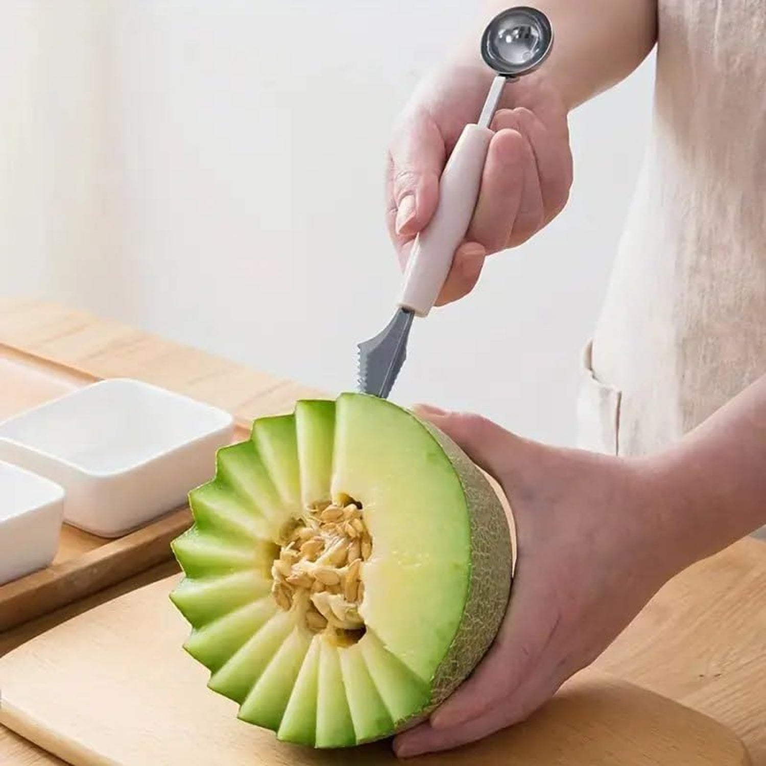 A person uses the carving end of a pink-handled 2-in-1 tool to create a decorative edge on a cantaloupe.