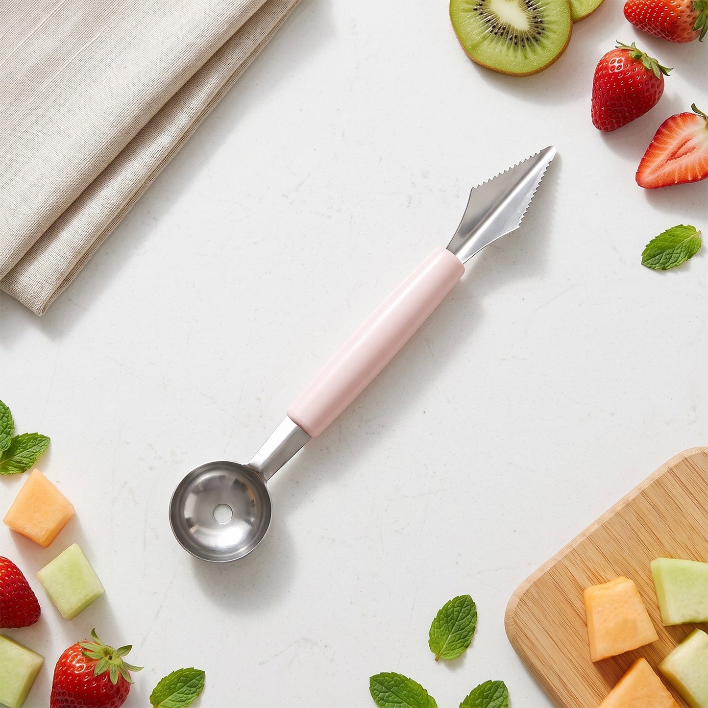 A pink-handled 2-in-1 fruit carving tool surrounded by various cut fruits and mint leaves on a white surface.