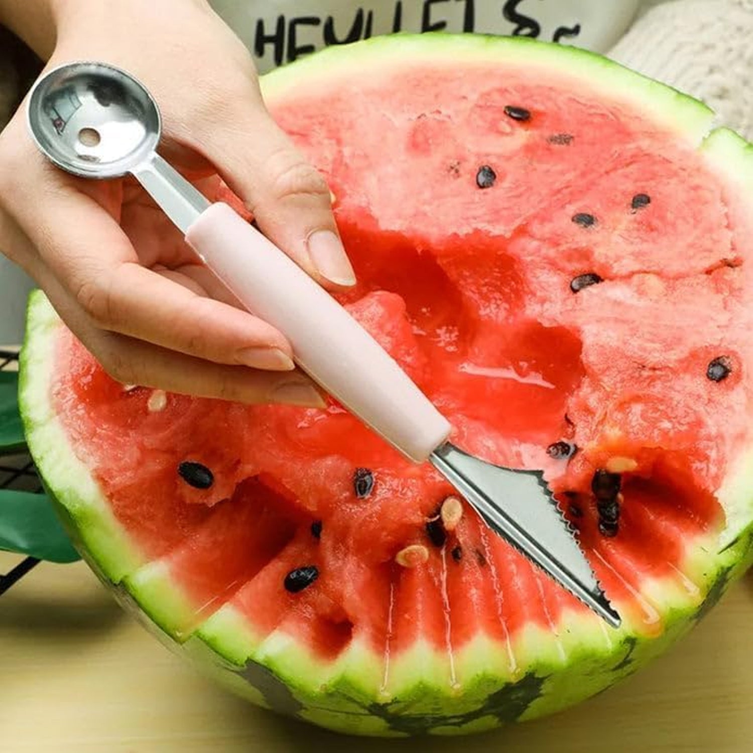 A person uses the carving end of a pink-handled 2-in-1 tool to cut a watermelon, revealing its red flesh.