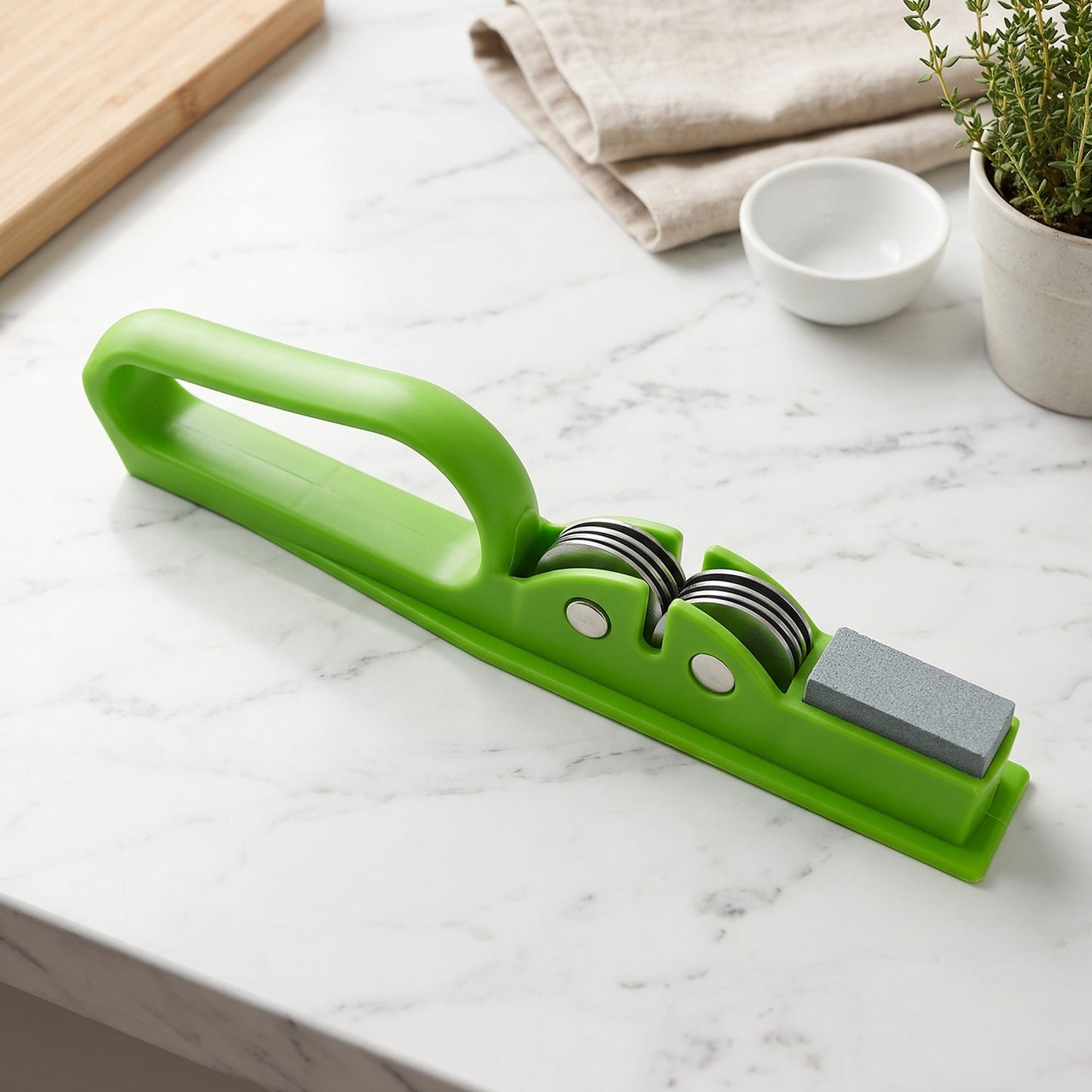 A green handheld knife sharpener on a white marble countertop with a wooden cutting board and a small plant in the